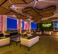 THE RIVIERA WONGAMAT BEACH PATTAYA - Luxusný bytový priestor s výhľadom na večerné osvetlenie mesta, zelenou stenou a pohodlným sedením.
