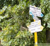 Dve susediace záhrady –12 árov v Stupave, s potenciálom na rekreáciu a - Turistické smerovníky obklopené lístím v Záhradách Malaciek, ukazujúce turistické trasy.
