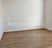 1 - izbový byt na prenájom v širšom centre LC - Prázdna miestnosť s drevenou podlahou v 1-izbovom byte, bledé steny a zásuvka.