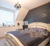 Predaj rodinného domu, Malacky - Spálňa v rodinnom dome s dekoratívnou tapetou, elegantným lusterom a oknami so žalúziami.