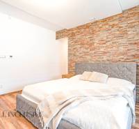 NA PREDAJ NADŠTANDARDNÁ 4-IZB. NOVOSTAVBA, DUN. KLÁTOV - Spálňa v rodinnom dome s kamennou stenou, elegantnou posteľou a dekoratívnymi doplnkami.
