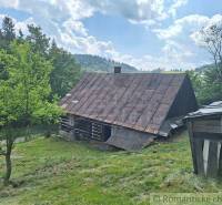 Drevenica v prírodnom prostredí, na okraji obce Zákopčie. - Drevená chata v Zákopčí na svahu, obklopená stromami a modrou oblohou.