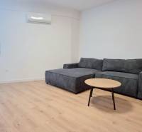 BÝVAJ PRVÝ v 2i byte, DIAMNAT, BALKÓN, KLÍMA, PARKING, Rybničná ulica - Obývacia izba s rohovou sedačkou, drevenou podlahou a minimalistickým stolíkom v 2-izbovom byte.