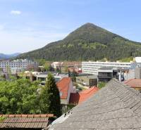 Rodinný dom v rekonštrukcii, Ružomberok - Na ulici Nám. A. Hlinku vidieť strechy, budovy a zalesnený kopec poza Rodinný dom.