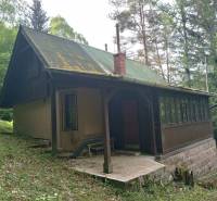 Na predaj chata pri jazere v Sklených Tepliciach - Chata na ulici Sklené Teplice, obklopená lesom, vidno strechu a verandu.