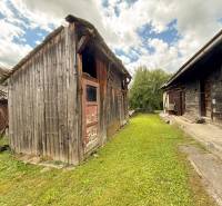 Exkluzívne na predaj drevenica s pozemkom 406 m2, Papradno - Drevené budovy pri chate v Papradne, obklopené zeleňou a modrou oblohou.