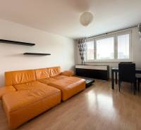 Priestranný 3-izbový byt s balkónom 68 m² Belinského - Obývačka v 3-izbovom byte s oranžovou sedačkou, čiernymi policami a jedálenským stolom.