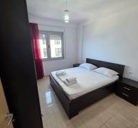 Sarandë - zariadený apartmán s otvoreným výhľadom na more - Spálňa v rekreačnom apartmáne s dvojlôžkom, nočnými stolíkmi a oknom s červenými závesmi.