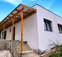 ‼️ NOVO POSTAVENÝ RODINNÝ DOM  S GARÁŽOU NA PREDAJ, MALÉ KRŠTEŇANY  ‼️ - Rodinný dom v Malých Kršteňanoch s drevenou prístavbou a betónovými schodmi, modrá obloha.