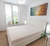 Jedinečný 3-izbový apartmán s balkónom, 71 m², Nový Ružinov - Spálňa v 3-izbovom byte s veľkou posteľou, obrazom a kvetmi na parapete.