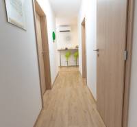 Jedinečný 3-izbový apartmán s balkónom, 71 m², Nový Ružinov - Chodba s drevenou podlahou, vedúca k zeleným barovým stoličkám v 3-izbovom byte.