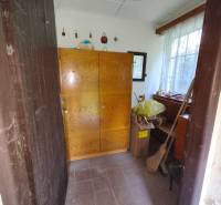 CHATA KORDÍKY - 2 poschodia, 3 izby+kuchynka, kúpelňa - 420 m2 pozemok - Interiér chaty s drevenou skriňou a oknom, vedľa kartónových škatúľ a metly.