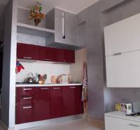 Predaj bytu 3-izbového (3+kk) s rozlohou 65 m² a terasou 10 m², Scalea - Kuchynská linka v 3-izbovom byte s lesklými červenými skrinkami a dekoráciou na poličke.
