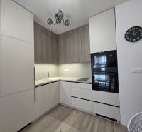 PRENÁJOM, 1.5 IZBOVÝ BYT, CÉDROVÁ UL., KOŠICE - Kuchyňa v 2-izbovom byte s bielymi a drevenými skrinkami, zabudované spotrebiče, hodiny.
