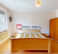 Predaj rodinného domu v Ivanke pri Dunaji - Spálňa v rodinnom dome s drevenou podlahou, posteľou a oknom s výhľadom do záhrady.