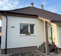 ? Na predaj: Rodinný dom s vedľajšou stavbou – Trstin (okres Trnava) - Rodinný dom v Trstíne s bielou fasádou, hnedou strechou a vydláždeným chodníkom.
