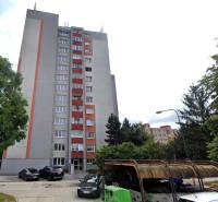 Predaj 3i byt, nepriechodné izby, výhľad, jazero Dražiak, Petržalka - Bytový dom na Krásnohorskej v Bratislave - Petržalka so zaparkovanými autami a stromami.