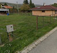 PREDAJ SP V ČASTEJ - 691 m2  ,,, ZNÍŽENÁ CENA,,, - Na ulici Slnečná pozemky: Trávnik, dom, oplotenie, budovy a stromy v pozadí.