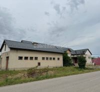 Dobré reality - Polyfunkčný objekt na predaj - Budova v Tekovských Lužanoch s trávnatým okolím pri ceste pod zamračenou oblohou.