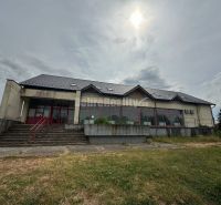 Dobré reality - Polyfunkčný objekt na predaj - Budova v Tekovských Lužanoch s veľkými oknami a schodiskom, obklopená trávnatou plochou.