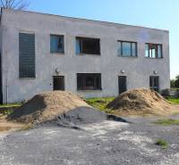 Na predaj sklady v obci Chrastince, Veľký Krtíš - Dvojpodlažná budova so štyrmi oknami a kopami štrku na ulici Chrastince.