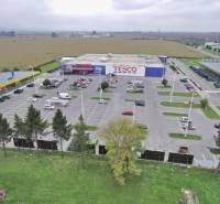 Obchodné priestory na prenájom v nákupnom centre RGB Javorina - Obrázok zobrazuje obchodné priestory na ulici Trenčianska s parkoviskom a okolitou krajinou.