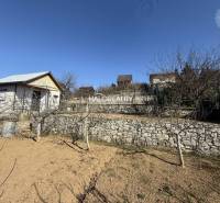 Predaj, záhradná chata Brodzany, pozemok 700 m2 - EX... - Záhrada s ovocnými stromami, kamenný múr, malý dom a modrá obloha.