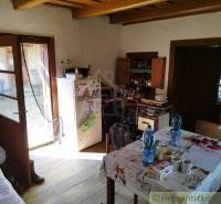 Veľký, vyše 4,5Ha slnečný pozemok s chalupou v strede, na lazoch, pri  - Kuchyňa na chate s dreveným dekorom, stolom so základnými potrebami a dverami do záhrady.