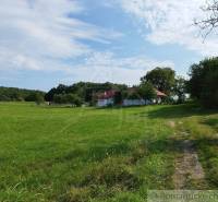 Veľký, vyše 4,5Ha slnečný pozemok s chalupou v strede, na lazoch, pri  - Chata pri Hrušove obklopená lúkou a stromami pod modrou oblohou.