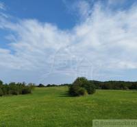 Veľký, vyše 4,5Ha slnečný pozemok s chalupou v strede, na lazoch, pri  - Lúka v Hrušove obklopená lesmi, pod modrou oblohou s oblakmi.