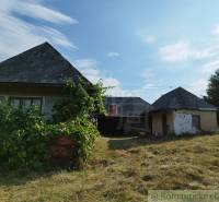 Veľký, vyše 4,5Ha slnečný pozemok s chalupou v strede, na lazoch, pri  - Chata v Hrušove obklopená zeleňou, staršia architektúra, strmé strechy na pozadí modrej oblohy.