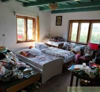 Veľký, vyše 4,5Ha slnečný pozemok s chalupou v strede, na lazoch, pri  - Izba v chate s posteľami, stolíkom a podlahou s dreveným dekorom.