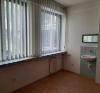 Prenájom kancelárií 21 m2 v centre Trnavy - Kancelária s umývadlom a podlahou s dreveným dekorom, svetlo cez vertikálne žalúzie.