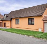 5-izbový rodinný dom s dvomi garážami v obci Špačince - Rodinný dom na ulici v Špačinciach so sedlovou strechou a oranžovou fasádou.