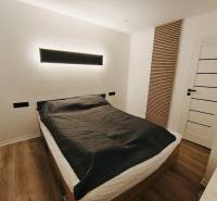 NA PRENÁJOM NOVOZREKONŠTRUOVANÝ 2-IZBOVÝ BYT, UL. ROŽŇAVSKÁ - Spálňa v 2-izbovom byte s posteľou, čiernymi detailmi a podlahou s dreveným dekorom.