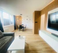 NA PRENÁJOM NOVOZREKONŠTRUOVANÝ 2-IZBOVÝ BYT, UL. ROŽŇAVSKÁ - Obývacia izba 2-izbového bytu s podlahou s dreveným dekorom, sedačkou a jedálenským kútom.