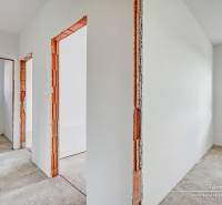 Novostavba 4-izbového rodinného domu v obci Slov.Nová Ves - Interiér rodinného domu s bielymi stenami a drevenými rámami dverí bez podlahovej krytiny.