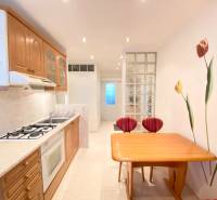 NA PRENÁJOM PRIESTRANNÝ 3-IZBOVÝ BYT V SKVELEJ LOKALITE, UL. SLOBODY - Kuchyňa v 3-izbovom byte s drevenými skrinkami, stolom a dekoratívnou stenou s kvetmi.