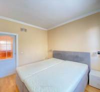 NA PRENÁJOM PRIESTRANNÝ 3-IZBOVÝ BYT V SKVELEJ LOKALITE, UL. SLOBODY - Spálňa s veľkou posteľou, nočnými stolíkmi a podlahou s dreveným dekorom v 3-izbovom byte.