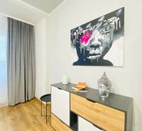 NA PRENÁJOM NADŠTANDARDNÝ 2-IZBOVÝ BYT V CENTRE MESTA - Interiér 2-izbového bytu s komodou, podlahou s dreveným dekorom a výrazným obrazom na stene.