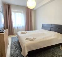 HD REALITY, Vám ponúka na Predaj 3-izbový Apartmán + Garážové státie - Spálňa so stolíkom, televízorom a podlahou s dreveným dekorom v 3-izbovom byte.