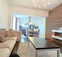 HD REALITY, Vám ponúka na Predaj 3-izbový Apartmán + Garážové státie - Obývačka v 3-izbovom byte s podlahou s dreveným dekorom, dekoratívnou stenou a krbom.