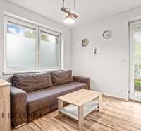 REZERVOVANÉ | NA PREDAJ 3-IZBOVÝ BYT S TERASOU, BLATNÁ NA OSTROVE - Obývačka v 3-izbovom byte s hnedou sedačkou a podlahou s dreveným dekorom.