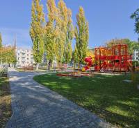 SEČOVSKÁ, 2-i tehlový byt, 56 m2, orientácia V a Z - OBKLOPENÝ ZELEŇOU - Detské ihrisko s červenými preliezačkami obklopené stromami na Sečovskej ulici v Ružinove, Bratislava.