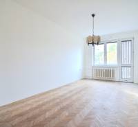 SEČOVSKÁ, 2-i tehlový byt, 56 m2, orientácia V a Z - OBKLOPENÝ ZELEŇOU - Obývacia izba s podlahou s dreveným dekorom v 2-izbovom byte ukazuje neutrálne biele steny.