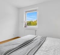 Slnečný 3i byt pod lesom, 74m2, balkón, parking, pivnica, Hainburg - Svetlá spálňa s bielymi stenami a posteľou, podlaha s dreveným dekorom, 3-izbový byt.