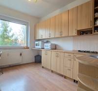 REZERVOVANÉ: NA PREDAJ -  1-izbový byt vo Veľkom Šariši - PREŠOV - Kuchyňa v 1-izbovom byte s podlahou s dreveným dekorom, drevenými skrinkami a veľkým oknom.