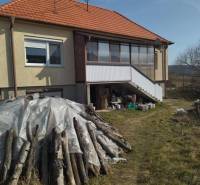 Rodinný dom v obci Dobrá Voda  - Rodinný dom v Dobrej Vode s drevenými polenami na oplocenom pozemku.