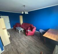 Veľký 2-izb. byt na ul. Vranovská, Petržalka, lodžia, 4.p./7 - Modrá garsónka s červenou pohovkou, stolíkom a podlahou s dreveným dekorom.