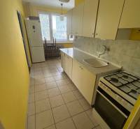 Veľký 2-izb. byt na ul. Vranovská, Petržalka, lodžia, 4.p./7 - Kuchyňa v garsónke so žltými stenami, bielymi skrinkami a sporákom.